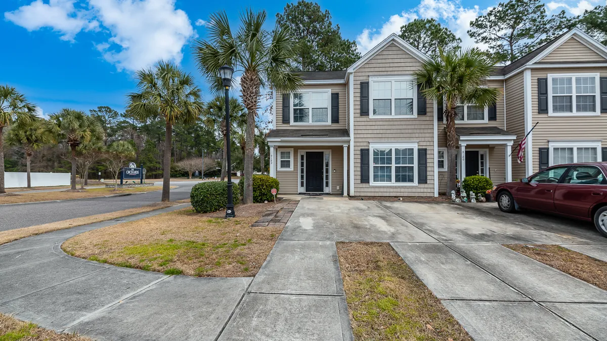 This exterior image shows the front entrance of the townhouse framed by palm trees, a driveway, and a car parked outside. The atmosphere is welcoming, with a well-maintained yard and inviting porch that suggests a comfortable home base for exploration and family relaxation.