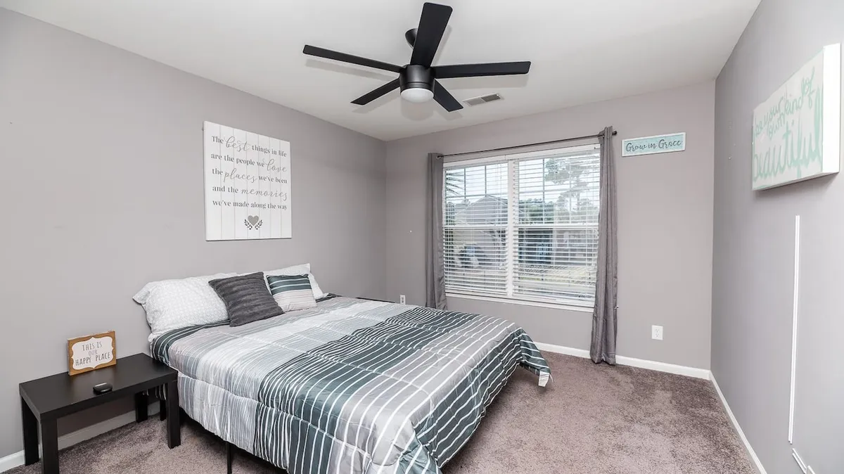 A peaceful bedroom space with striped bedding on the bed, a window letting in gentle natural light, and decorative wall art. The soft ambiance suggests a haven ideal for reading, meditating, or simply unwinding together.