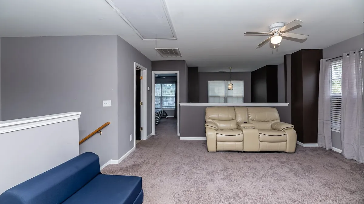 A spacious lounge area with beige recliner chairs and a blue accent chair, opening up to the kitchen, and arranged for group relaxation or entertainment. The open space is ideal for family movie nights or friendly gatherings, mirroring the flexible, communal spirit of the loft.