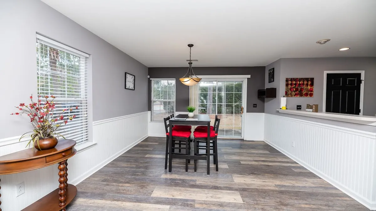 A stylish dining area with a modern table surrounded by bold red chairs, large windows letting in plenty of natural light, and colorful wall art to add personality. The setup is ideal for group meals, game nights, or celebrations.