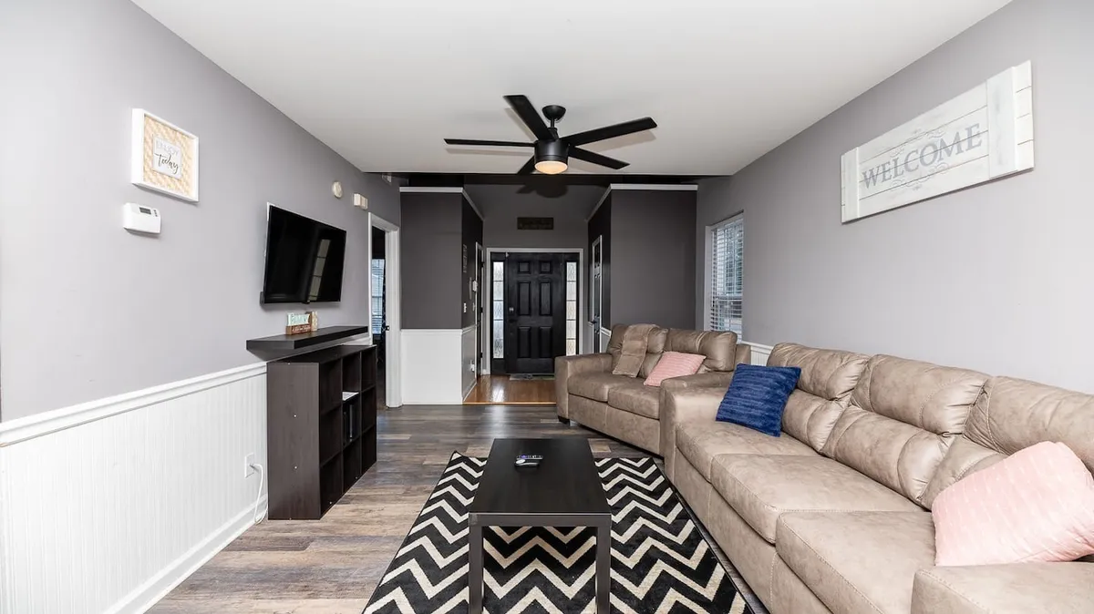 A bright living area is shown with a comfortable sofa, coffee table, television, and tasteful wall décor. The room is arranged for socializing, relaxing, or gathering for movie nights and group activities after a day out.