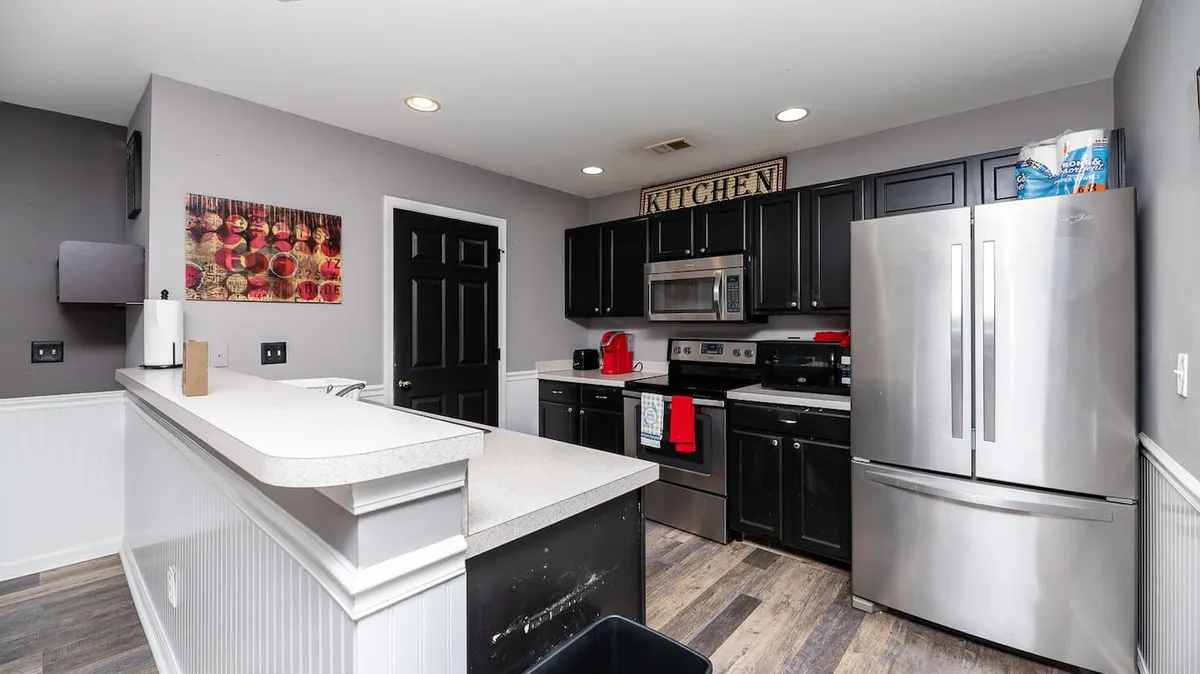 This image showcases the kitchen area featuring black cabinetry, stainless steel appliances, a central kitchen island, and a welcoming 'kitchen' sign. The setup is ideal for both cooking and socializing, offering ample space for meal preparation and gatherings.